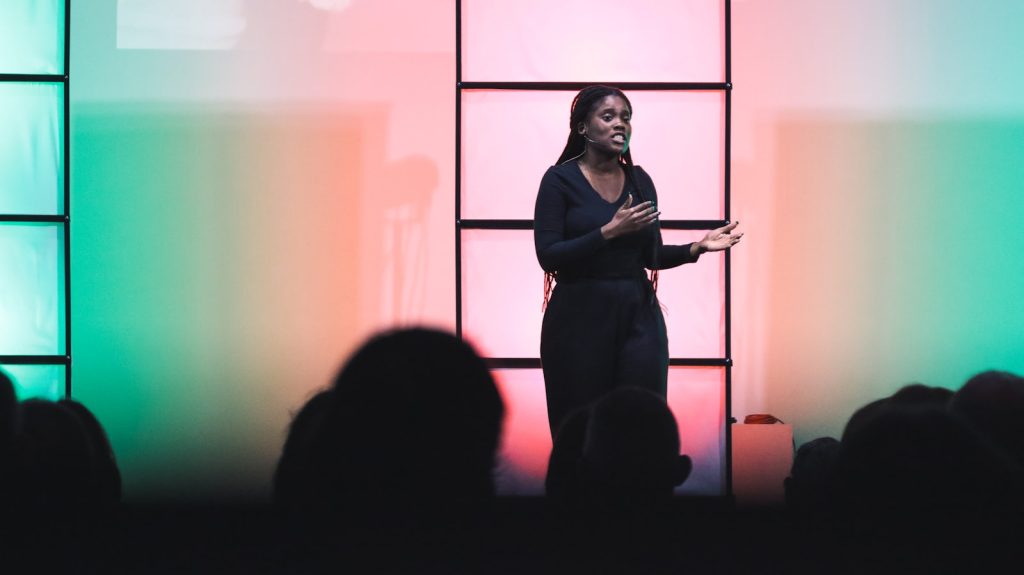 Dagvoorzitter met microfoon op een podium voor een volle zaal